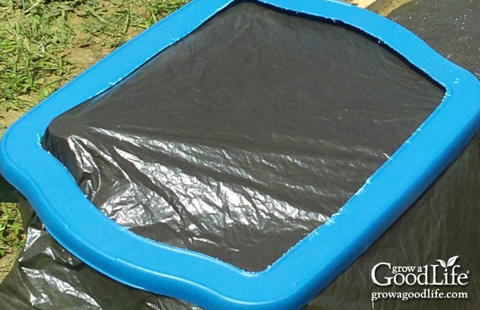 Plastic mulch layer secured over the top of a self-watering planter with the rim snapped into place.