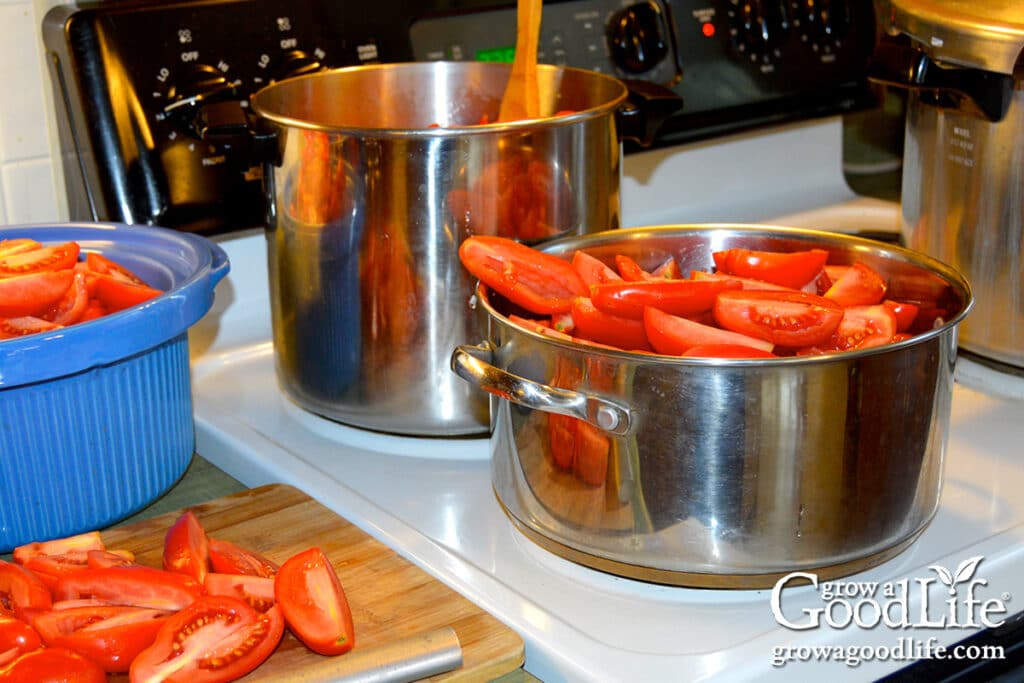 Two large pots filled with quartered tomatoes simmering on the stove to make homemade seasoned tomato sauce for canning.