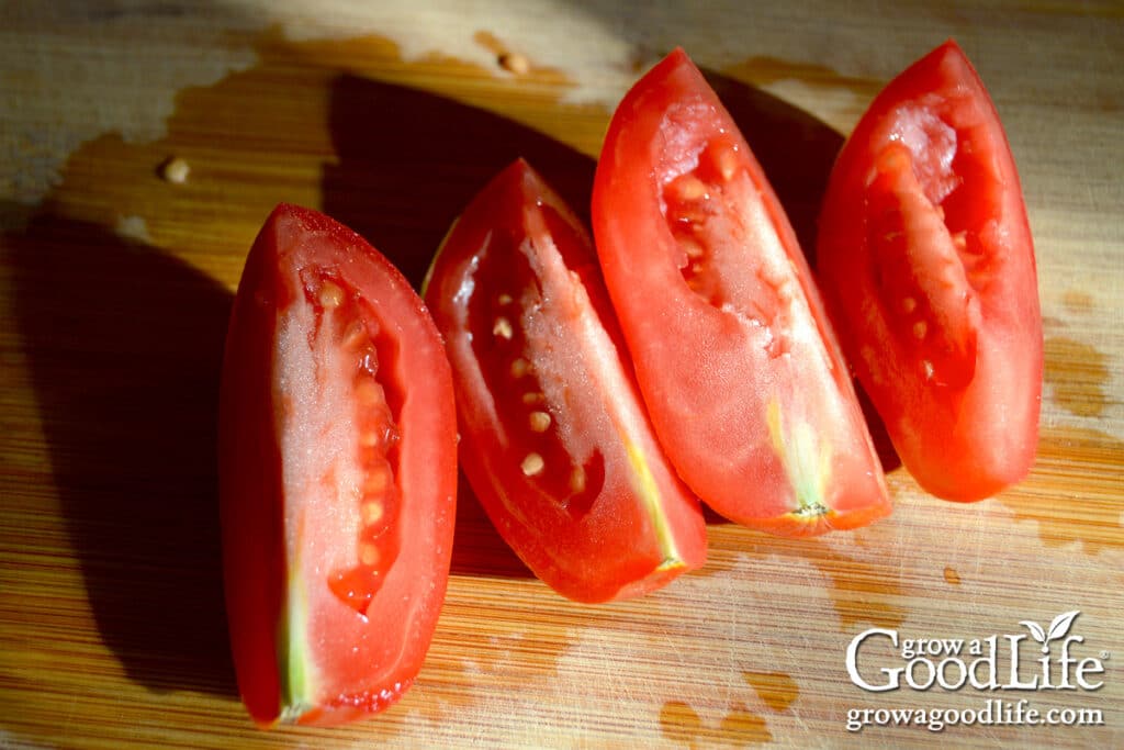 Fresh Roma tomatoes quartered on a cutting board, prepared for cooking into seasoned tomato sauce.