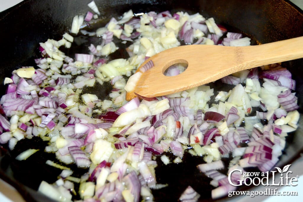 Sautéing chopped onions and minced garlic in a skillet as the base for homemade seasoned tomato sauce.