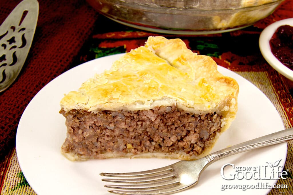 A slice of tourtiere, French meat pie on a white plate on a table.