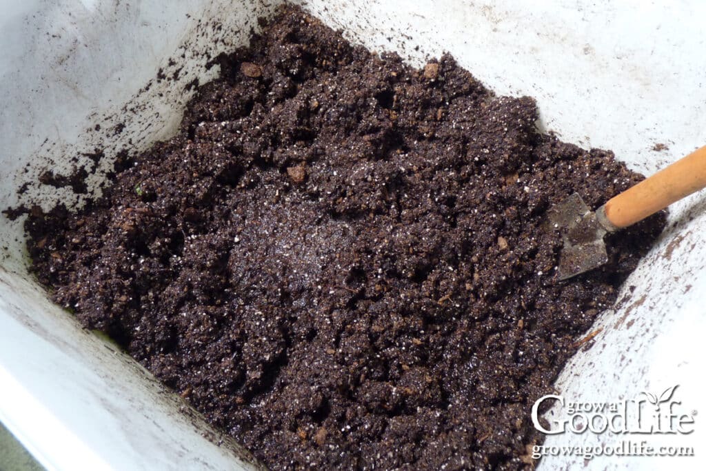 Overhead view of mixing seed starting mix with water in a container to prepare soil for planting seeds.