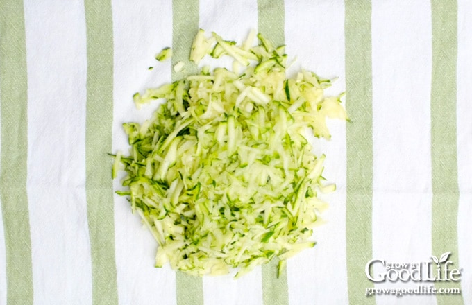 using a towel to squeeze out moisture from the shredded zucchini