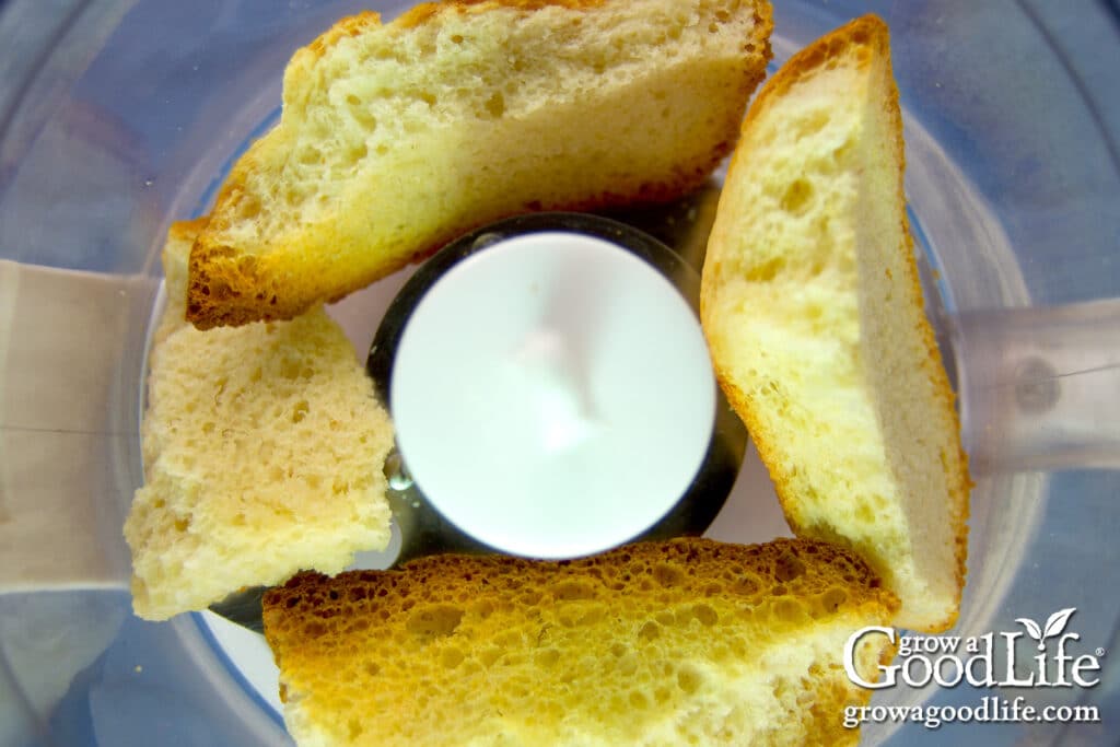 Dried bread pieces in a food processor ready to be pulsed into bread crumbs.
