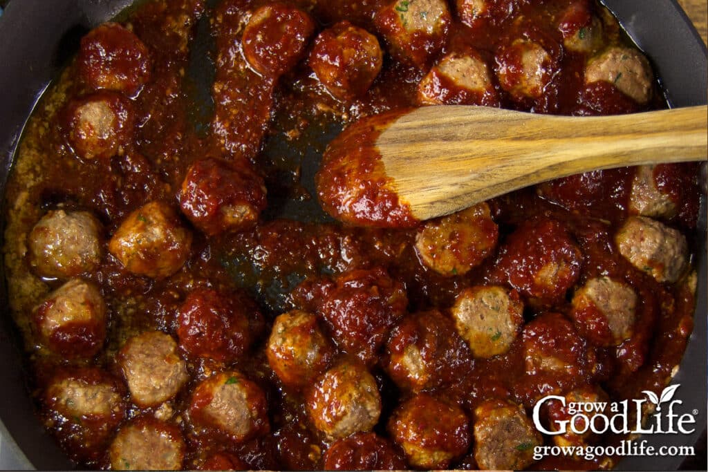 Meatballs simmering in thick homemade barbecue sauce in a skillet on the stovetop.