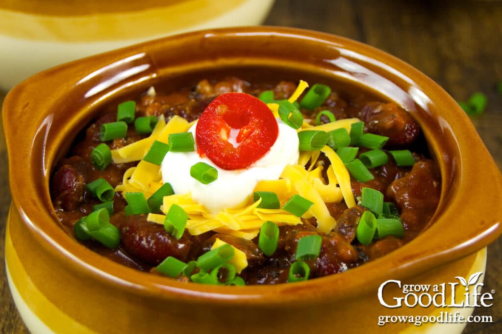A bowl of chili with toppings, including shredded cheese, sour cream, red jalapeño, and fresh chives.