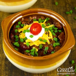Bowl of slow cooker chili topped with cheese, sour cream, red jalapeño, and fresh chives.