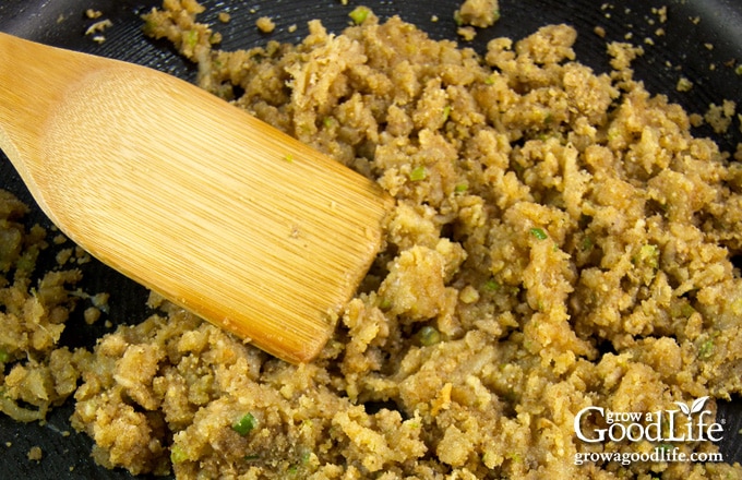 Garlic, cheddar, and breadcrumb mushroom stuffing in a black skillet with a wooden spoon.