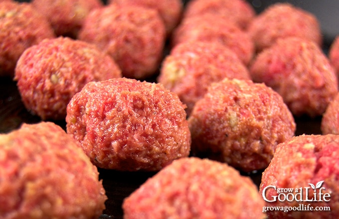 Meatballs browning in a skillet on the stovetop.