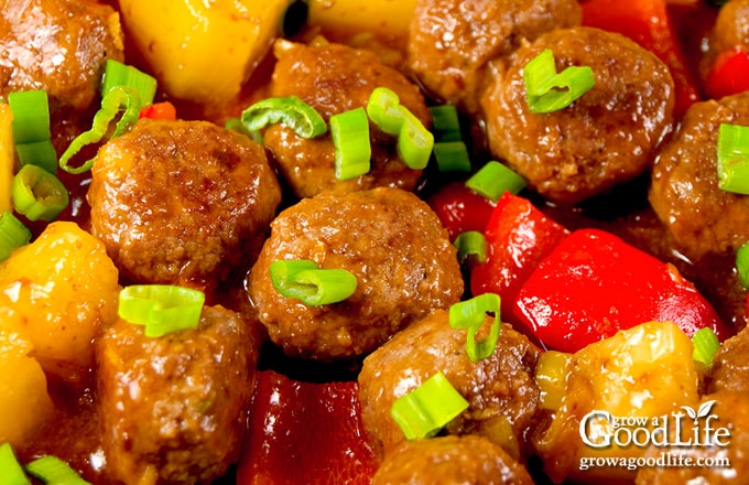 Sweet and sour meatballs with peppers and pineapple cooking in a skillet.