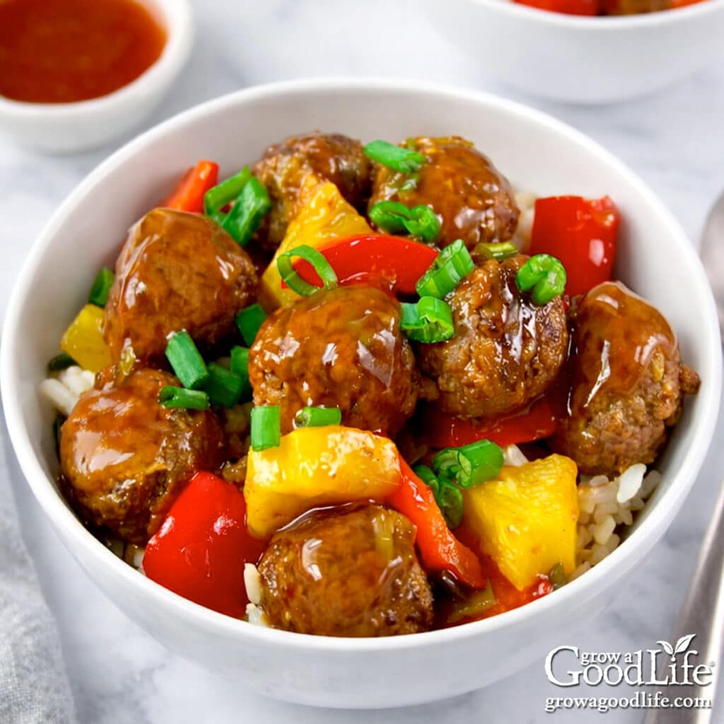 A bowl of sweet and sour meatballs with peppers and pineapple in a tangy sauce.