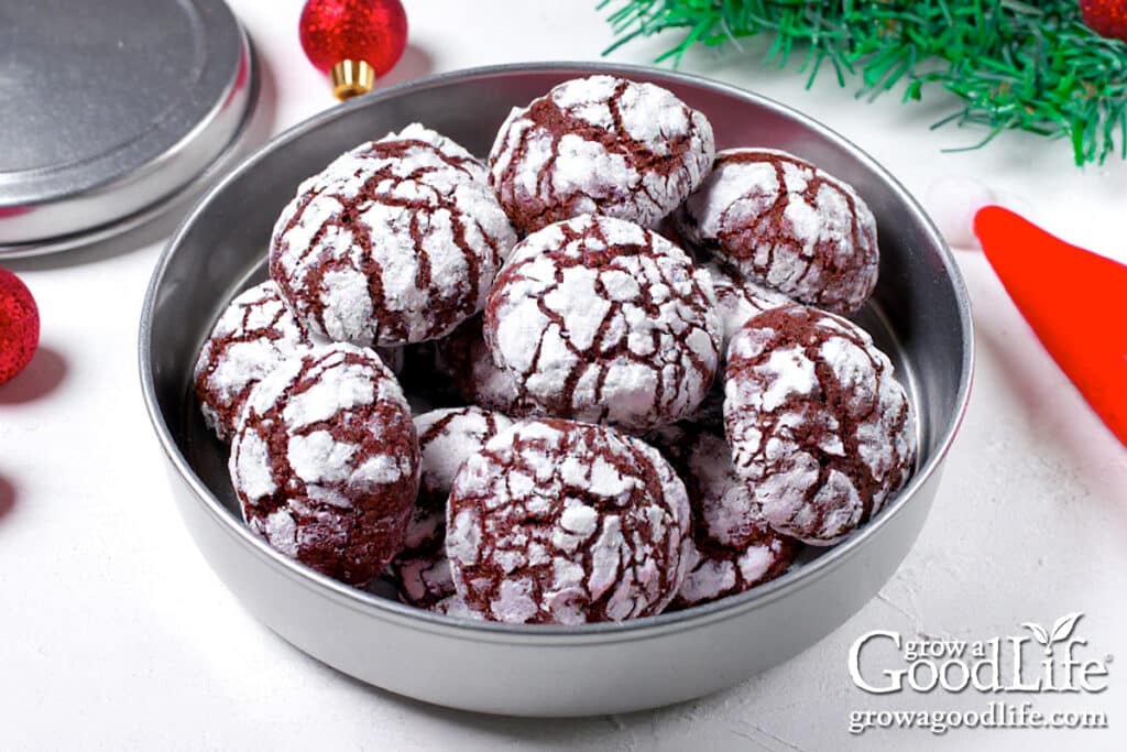A round cookie tin of chocolate crinkle cookies on a table.