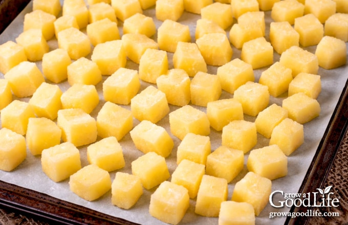 Blanched potato cubes spread on a parchment lined baking sheet ready to flash freeze.