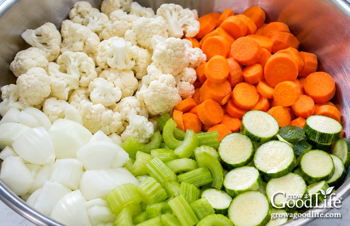 Prepared cauliflower, onions, celery, carrots, and zucchini grouped in a large stainless steel bowl for giardiniera.