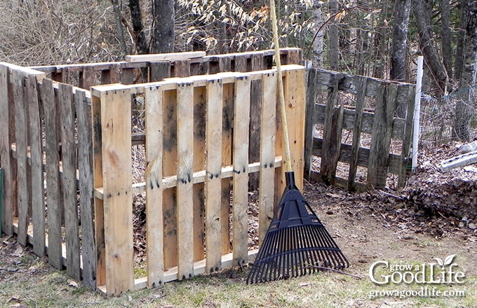 A rustic compost bin made of recycled pallets and fencing.