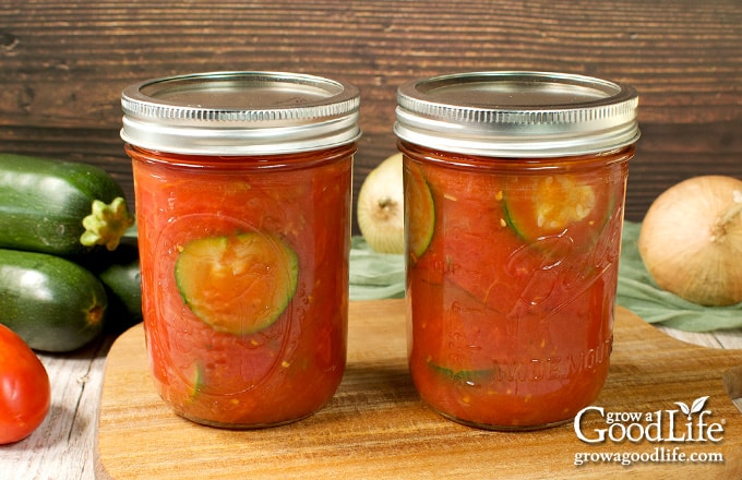 Jars of home canned zucchini with tomatoes on a table.