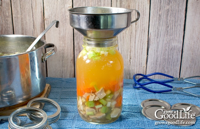 Filling a jar with solid soup ingredients and topping with turkey broth.