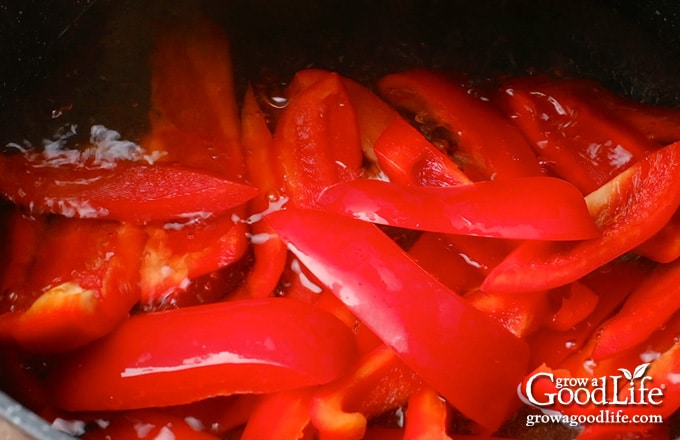 Adding prepared peppers to the pickling brine pot.