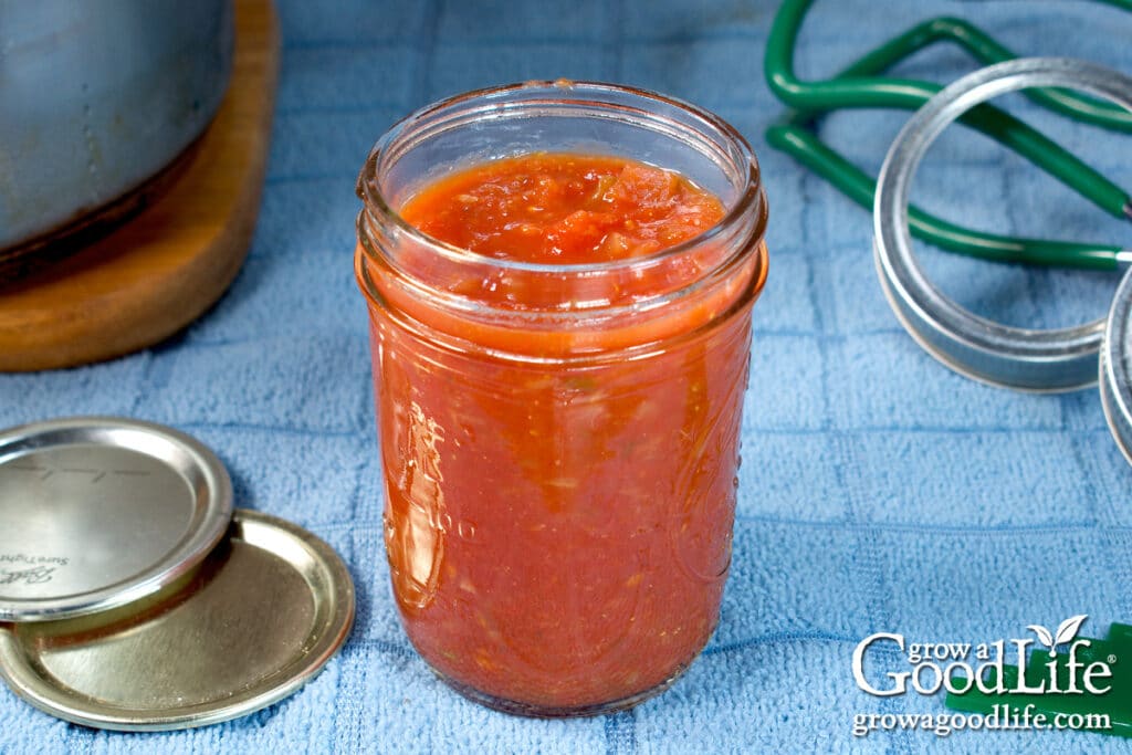 Filling a half-pint mason jar with hot salsa.