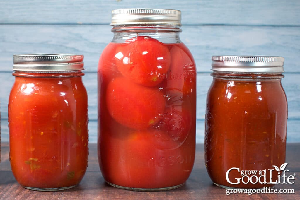 Jars of home canned tomato sauce, whole tomatoes, and stewed tomatoes on a counter.