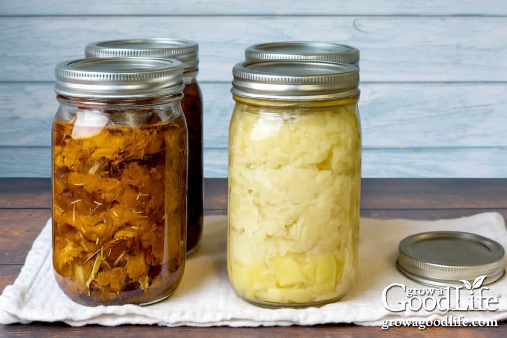 Four quart sized jars of pressure canned beef and chicken on a table.