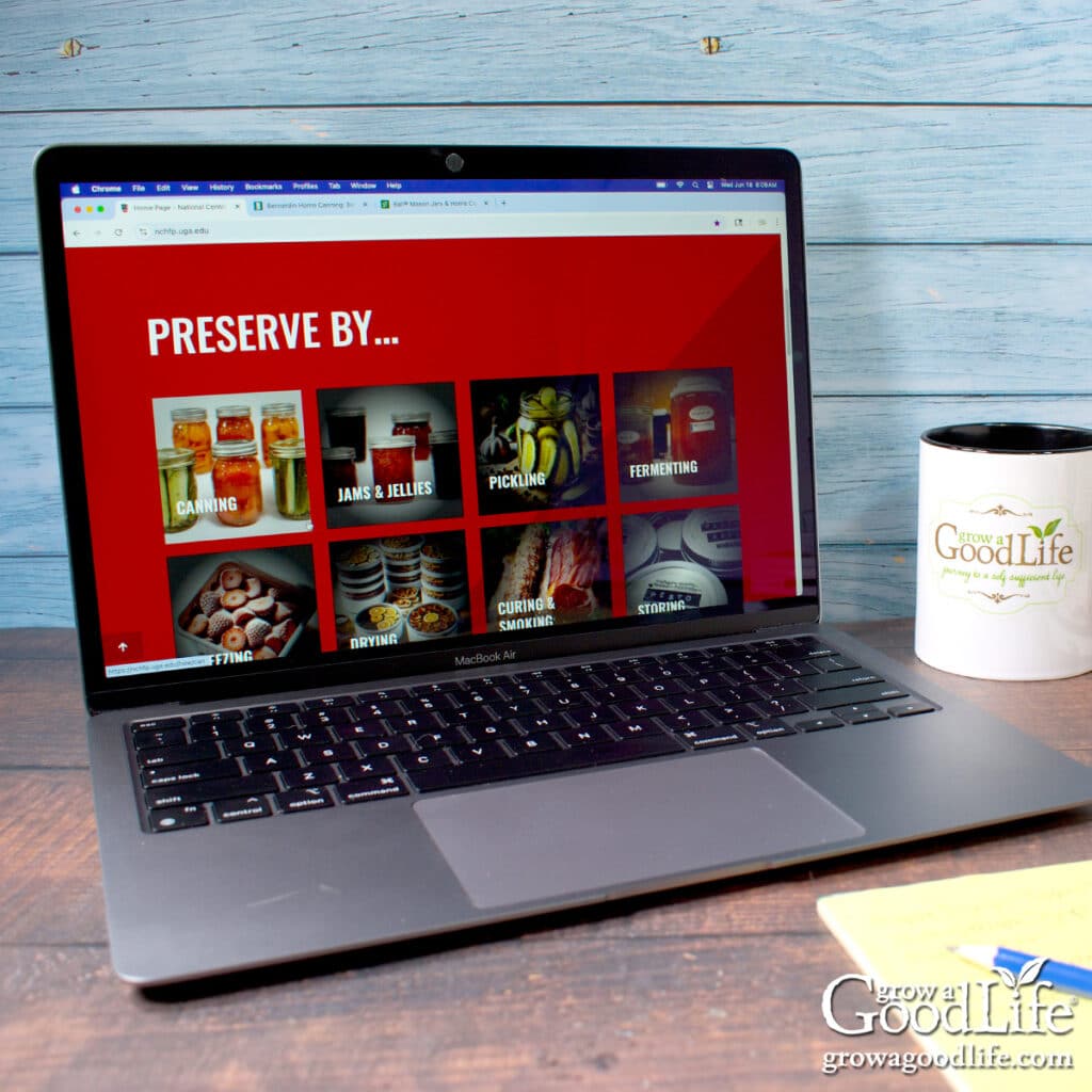 A desk with stacks of canning books and a computer with a canning website on the screen.