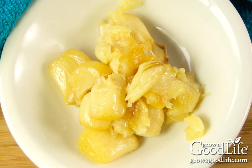 Small bowl of golden roasted garlic cloves ready to be added to homemade roasted tomato sauce.