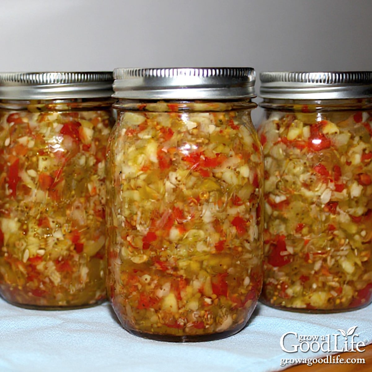 Jars of home canned spicy zucchini relish on a blue towel.