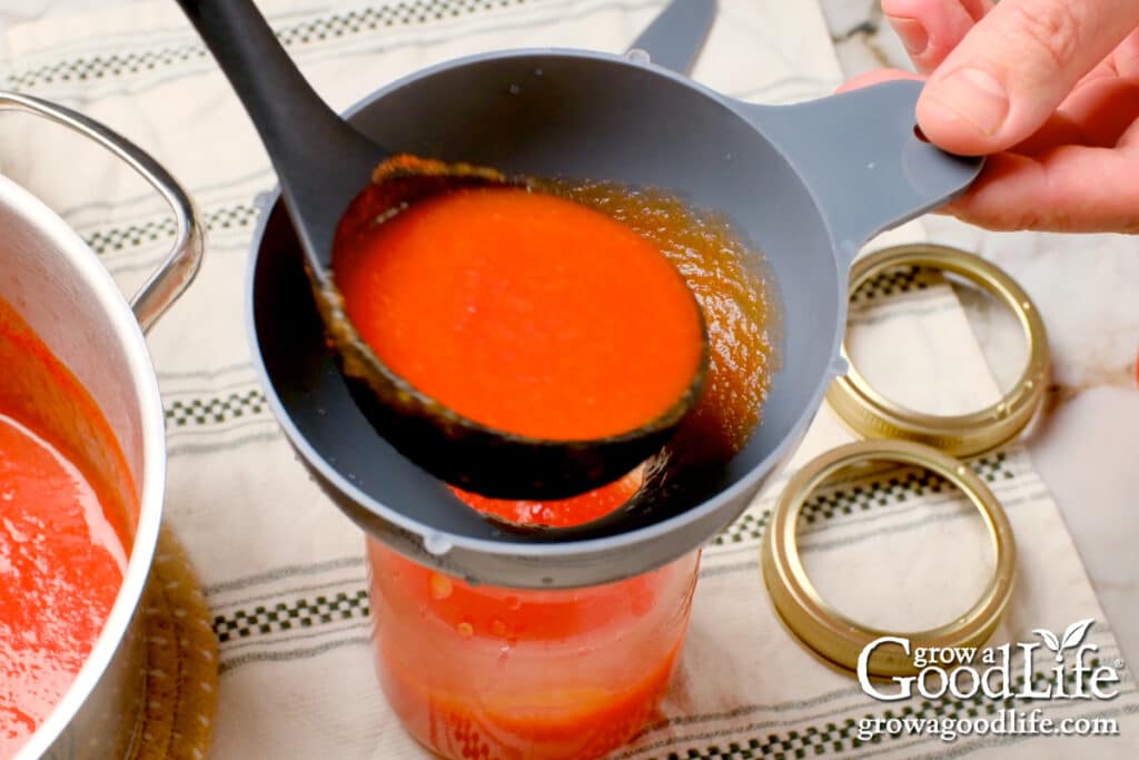 A ladle filling the jar with tomato sauce.