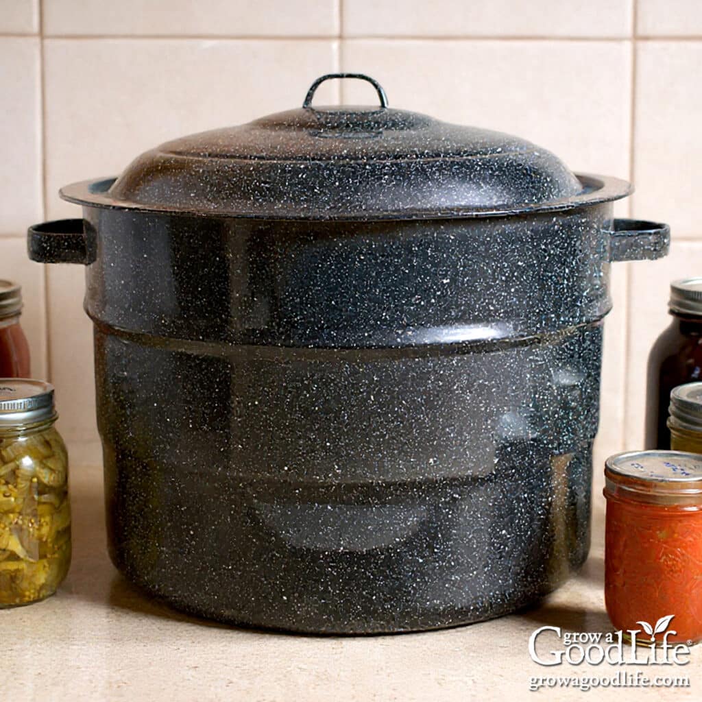 A water bath canner on a counter surrounded by jars of food.