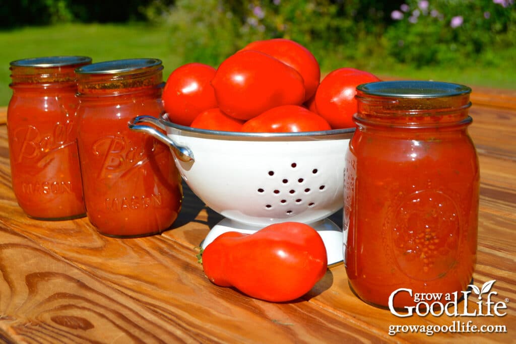 Three pint jars of home canned tomato basil sauce beside a bowl of fresh Roma tomatoes.