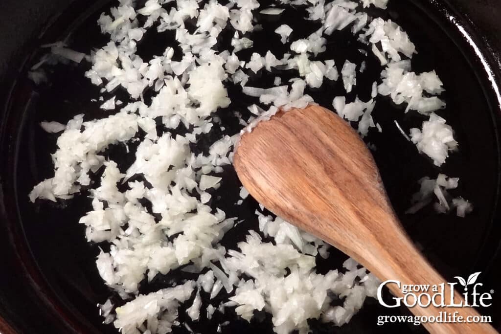 Chopped onions and minced garlic sautéing in olive oil in a skillet for tomato basil sauce.