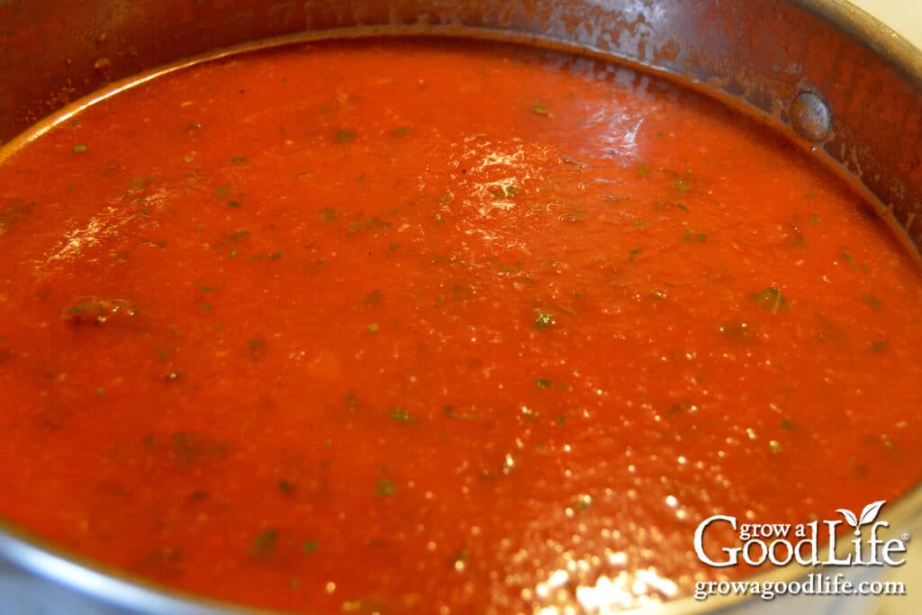 Tomato basil sauce simmering in a pot until thick and ready for canning jars.