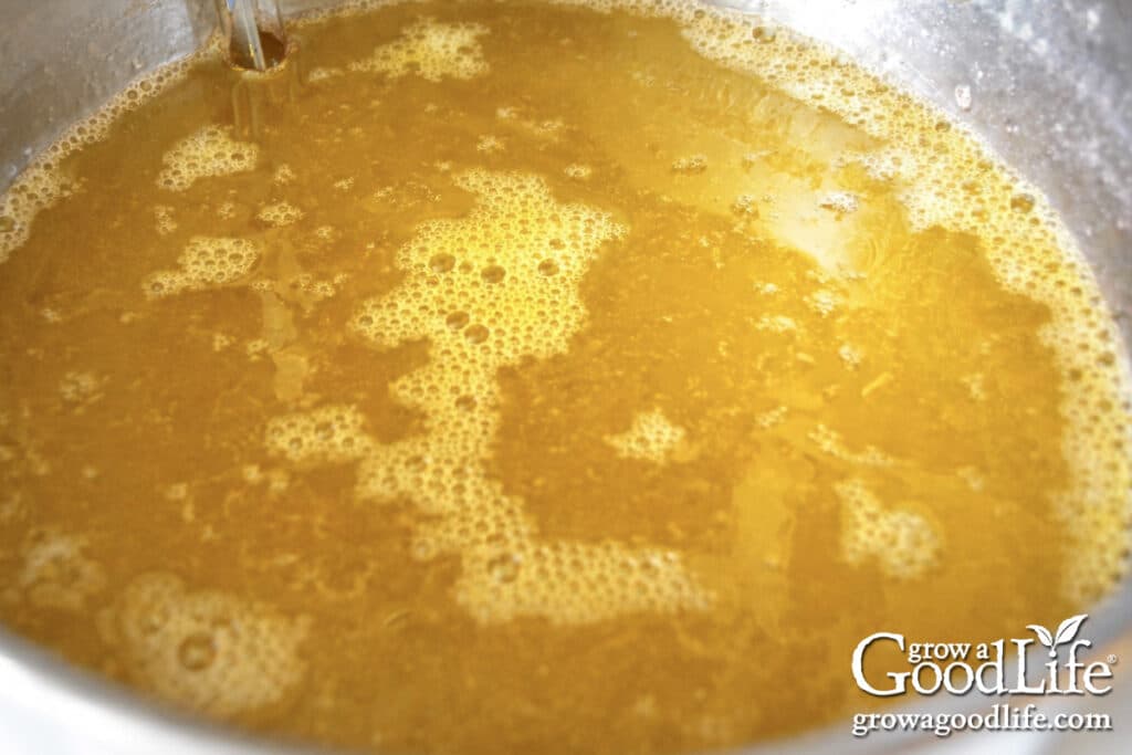 Dandelion jelly mixture coming to a boil in a stainless steel pot with golden liquid and foam forming on the surface.
