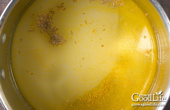 Golden bread and butter brine simmering in a pot with mustard seed, celery seed, turmeric, and peppercorns.