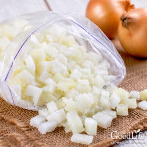 Freezer bag filled with frozen chopped onions on a table with whole yellow onions in the background.