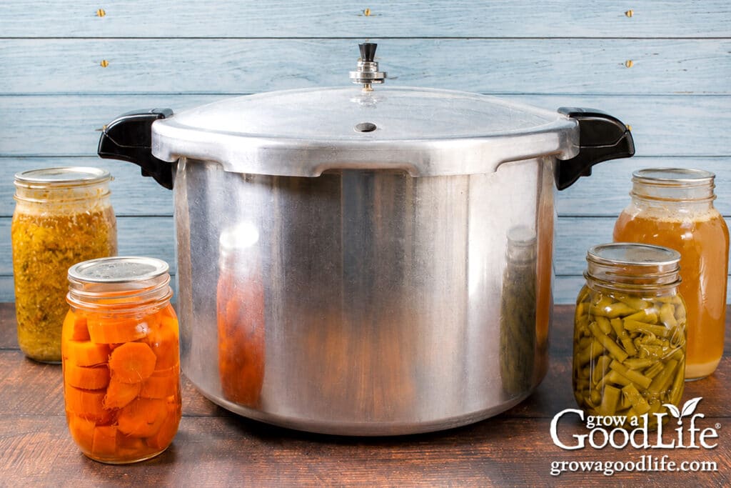 Presto pressure canner on a table with jars of pressure canned vegetables, chicken stock, and a meal in a jar.